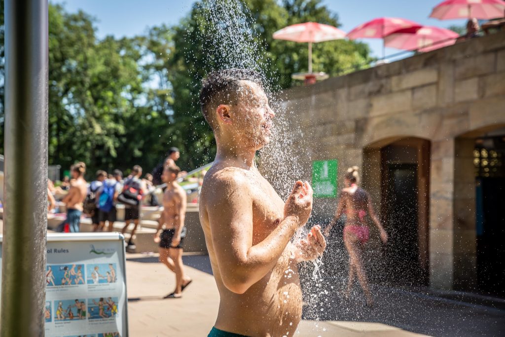 Zur Abkühlung stellt sich ein Freibadbesucher unter die kalte Außendusche