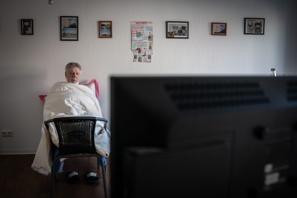 Da über Weihnachten die Heizung ausgefallen ist, sitzt ein Mann mit Decken und Kissen in seiner Wohnung