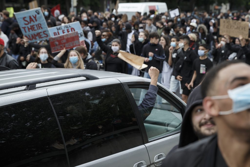 Der Beifahrer eines silbernen Kombis solidarisiert sich durch das heben seiner Faust mit einer vorbeiziehenden Black-Lives-Matter-Demo