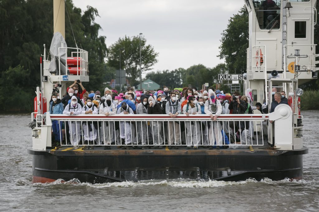 Umweltaktivisten in Maleranzügen überqueren einen Kanal mit einer Autofähre